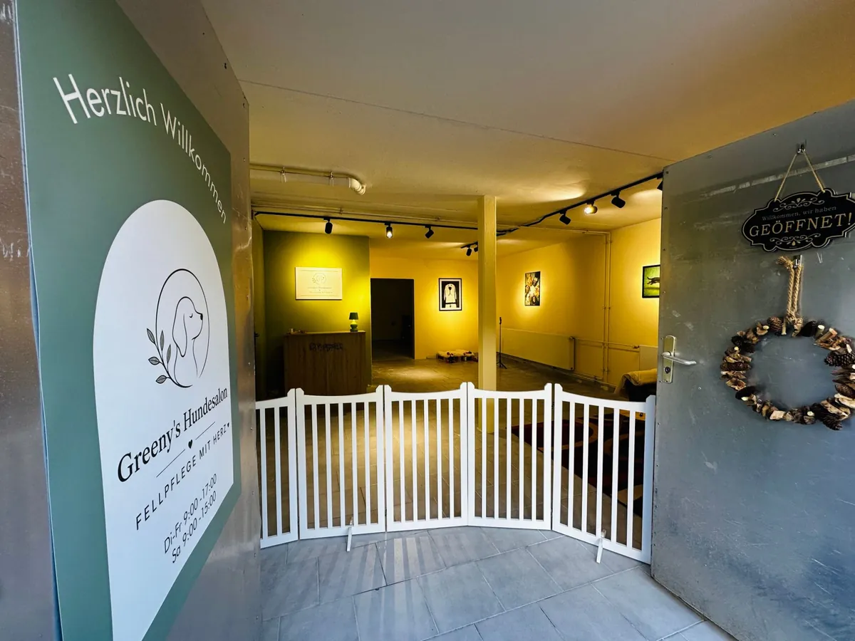 Eingang von Greeny's Hundesalon: grünes Schild „Herzlich Willkommen“ mit Logo und Öffnungszeiten, an der geöffneten Tür das Schild „Wir haben geöffnet“, dahinter ein weißes Hundegitter und der beleuchtete Empfang